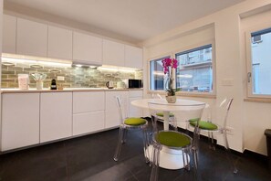 A modern kitchen with white cabinets, a tiled backsplash, and a round dining table with four chairs. - CASA INDIPENDENTE A PRATI (ROMA)