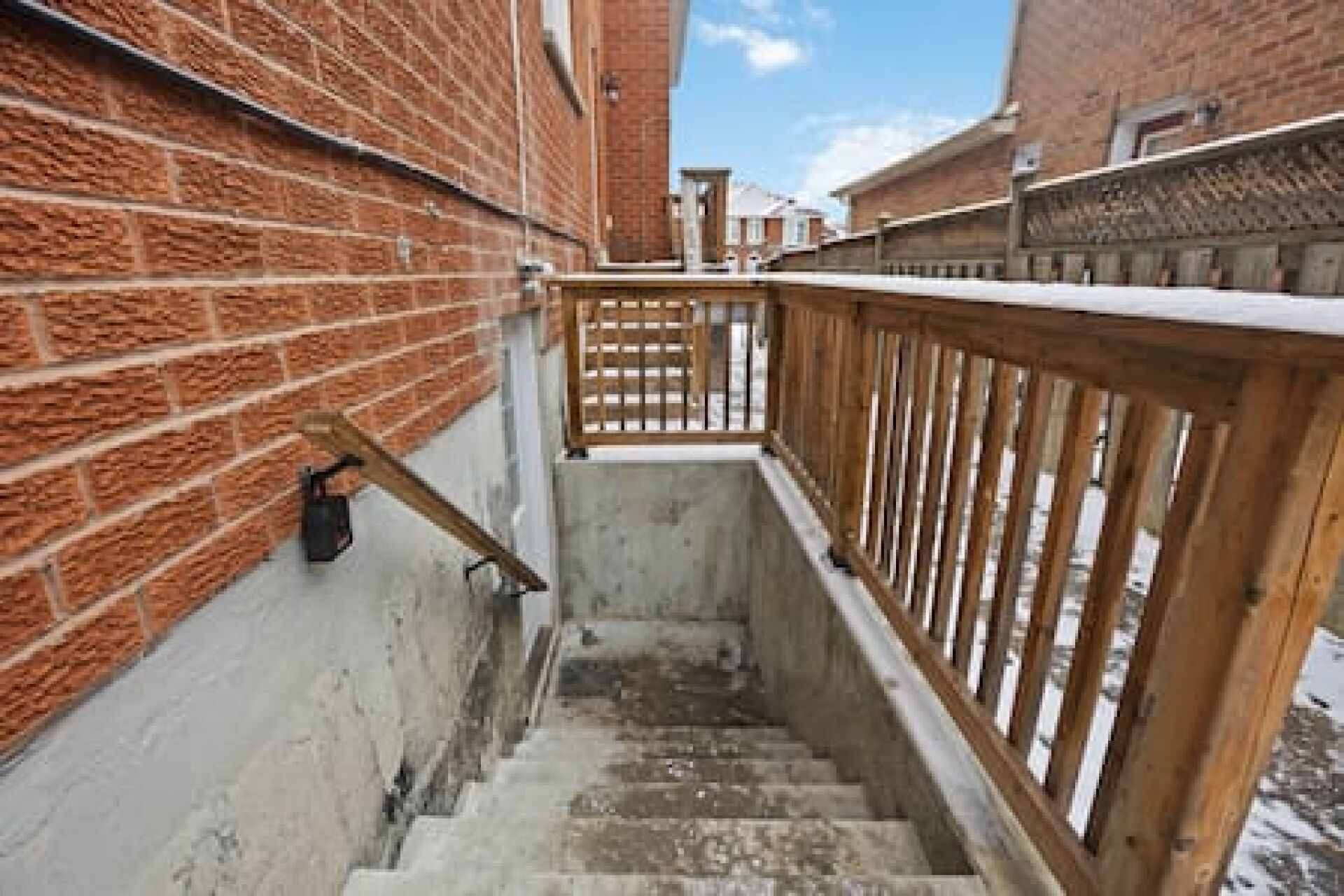 A narrow stairway with wooden railings, brick walls, and a concrete floor.