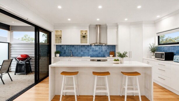 A modern kitchen with a large island, white cabinets, blue backsplash, and a sliding glass door leading to an outdoor area. - Mercer on Port - Your Perfect Portarlington Getaway (Portarlington)