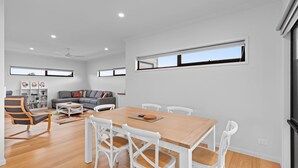 A modern living room with a dining area, white walls, and large windows. - Mercer on Port - Your Perfect Portarlington Getaway (Portarlington)