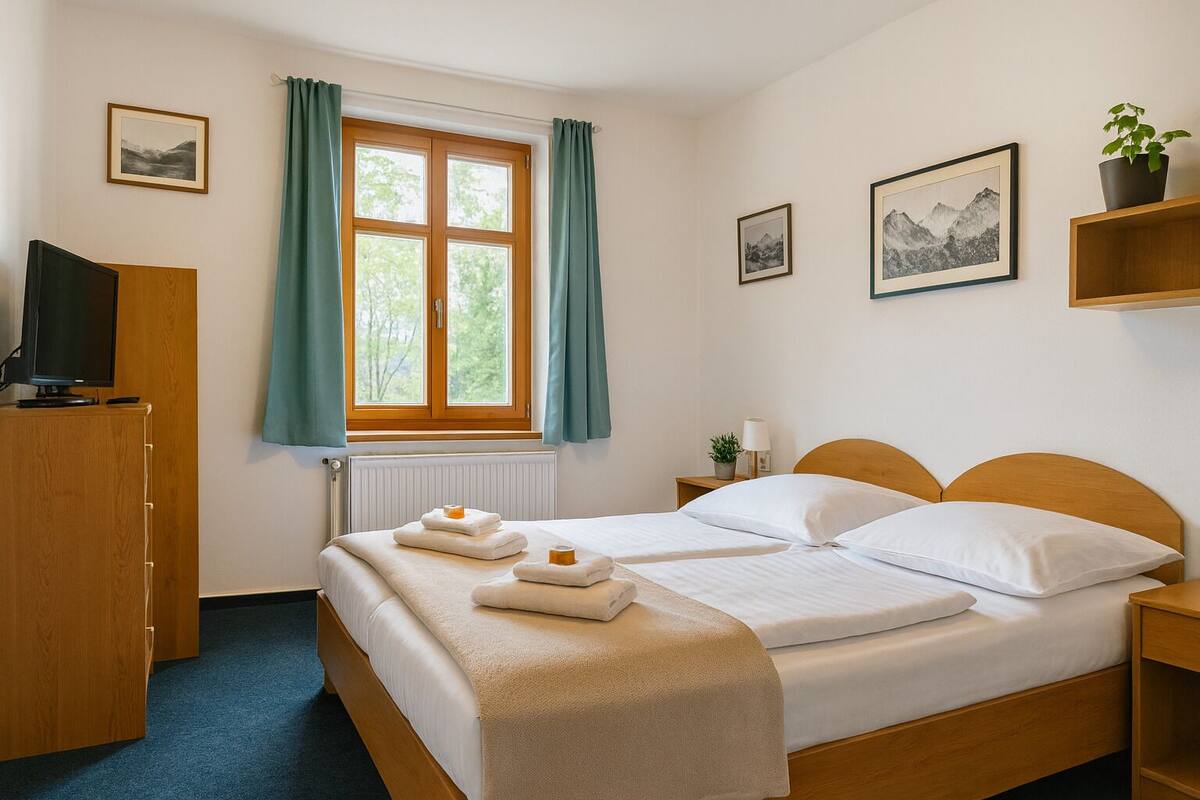 Una habitación de hotel con cama, escritorio, televisor y ventana con cortinas.