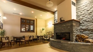 A cozy living room with a stone fireplace, wooden furniture, and a large window. - Hotel Franz - Rejvíz (Zlaté Hory)