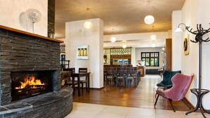 A spacious living area with a stone fireplace, wooden flooring, and a dining area with chairs and tables. - Hotel Franz - Rejvíz (Zlaté Hory)