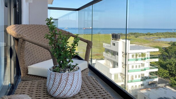 Ein Balkon mit Korbmöbeln, einem Blumentopf und Blick auf das Meer und Gebäude.