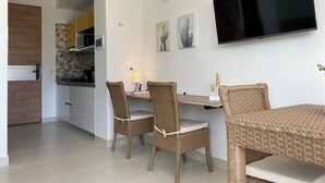 Eine moderne Küche mit weißen Schränken, einer eingebauten Mikrowelle und einem Herd. Es gibt einen Essbereich mit Korbstühlen und einem Tisch, einen flachbildschirmfernseher an der Wand und eine kleine Kakteendeko.