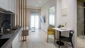 A modern kitchen with a built-in stove, a sink, and a dining area with a table and chairs. - Harma City Living - Street View Standard Apartment (Chania)