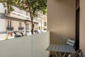 Ein Balkon mit Tisch und Stühlen, ein Baum sowie der Blick auf geparkte Autos und Gebäude.