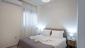 Un letto rifatto con lenzuola bianche, un comodino con una lampada e un condizionatore d'aria a parete.
