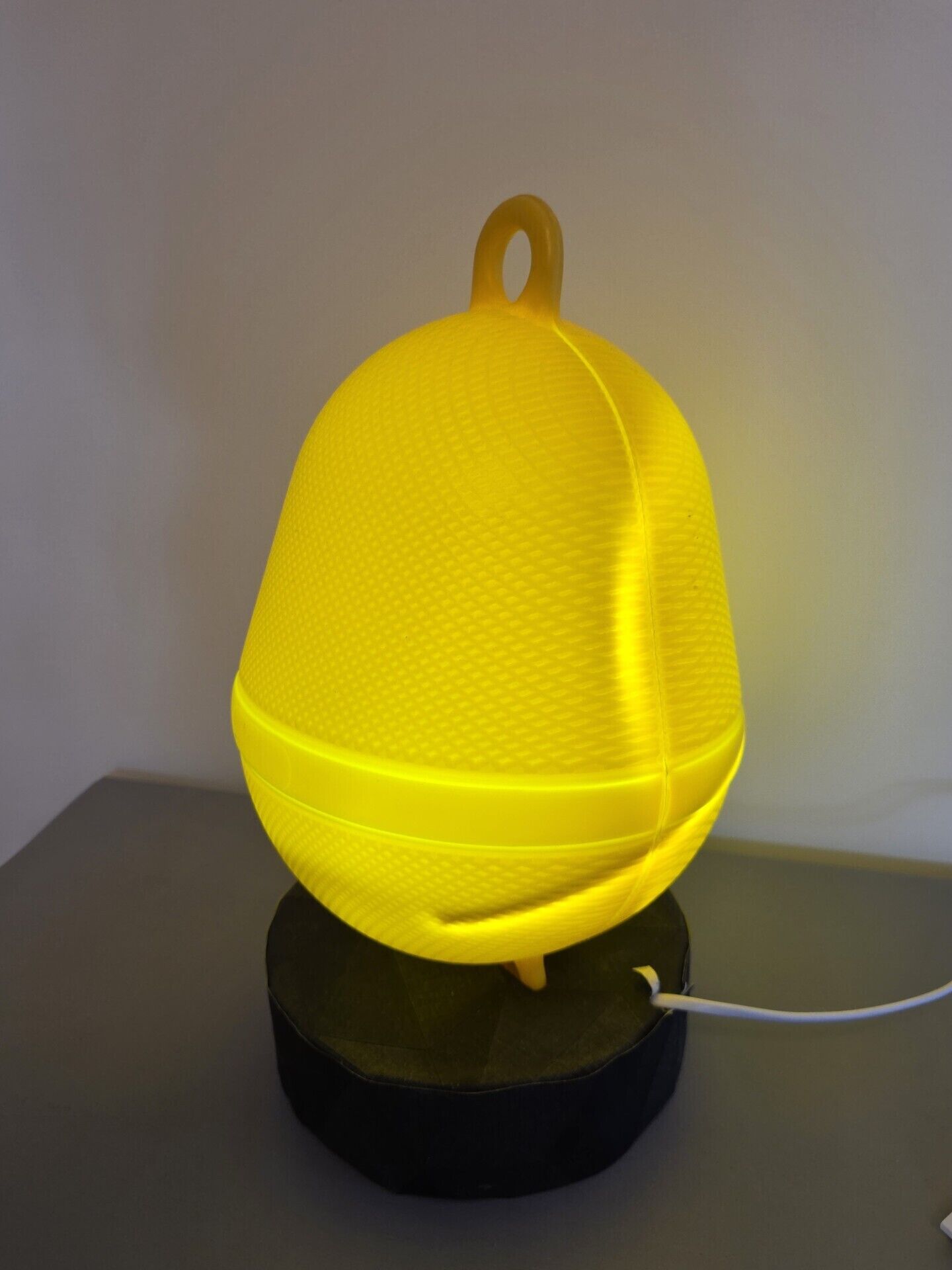 A yellow, textured, dome-shaped object with a handle, placed on a black circular base with a white cable connected to it.