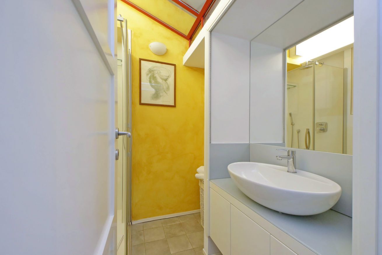 Une salle de bain avec un mur d’accent jaune, un lavabo blanc et une douche à parois de verre.