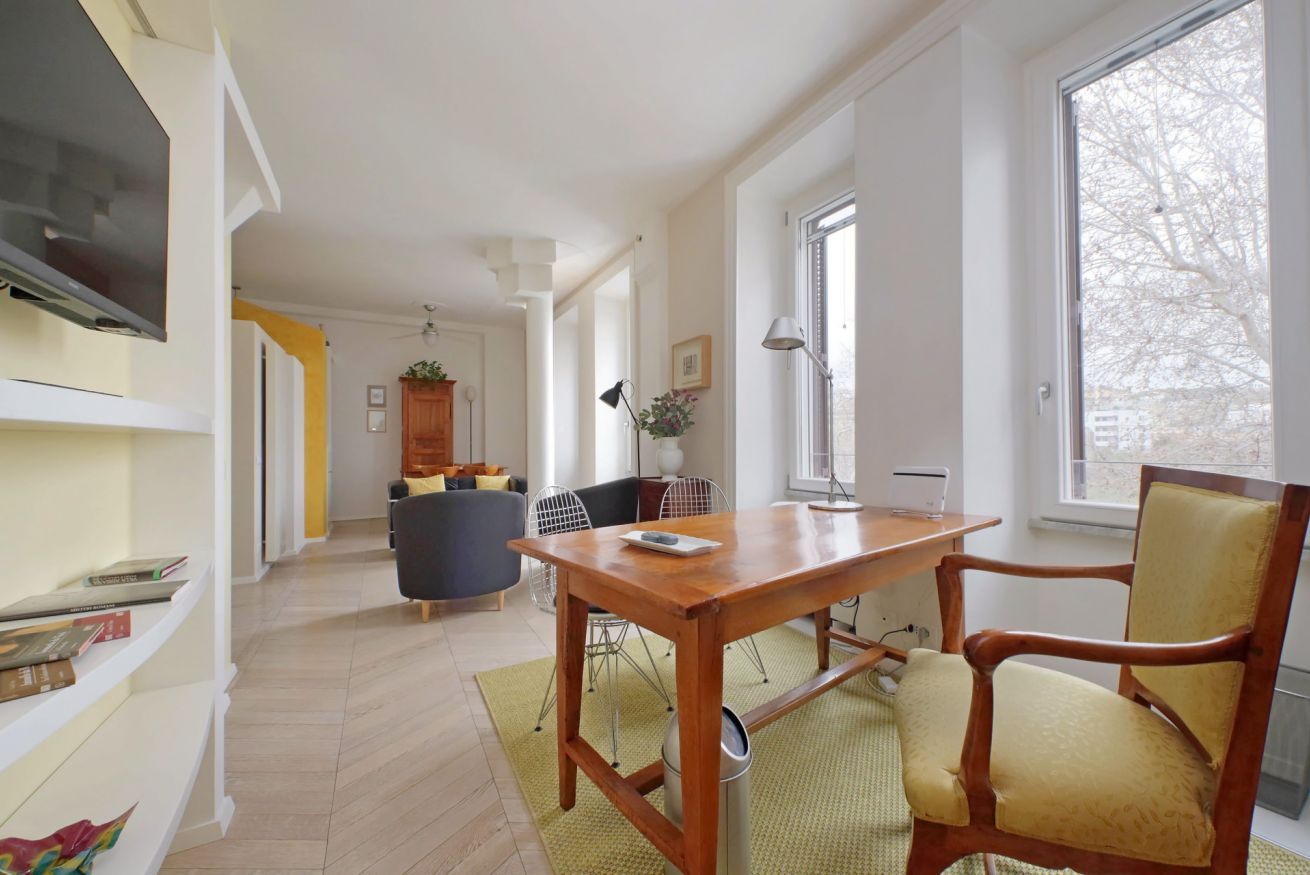 A modern living room with a wooden dining table, a comfortable sofa, and a TV mounted on the wall.
