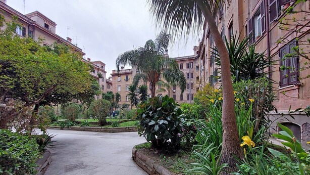Un sentiero che si snoda attraverso una zona residenziale con edifici su entrambi i lati, immerso nel verde e nella vegetazione.
