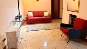 A living room with a red sofa, a glass coffee table, a white cabinet, a black armchair, and a fireplace. - Cangrande Apartment: city center (Verona)