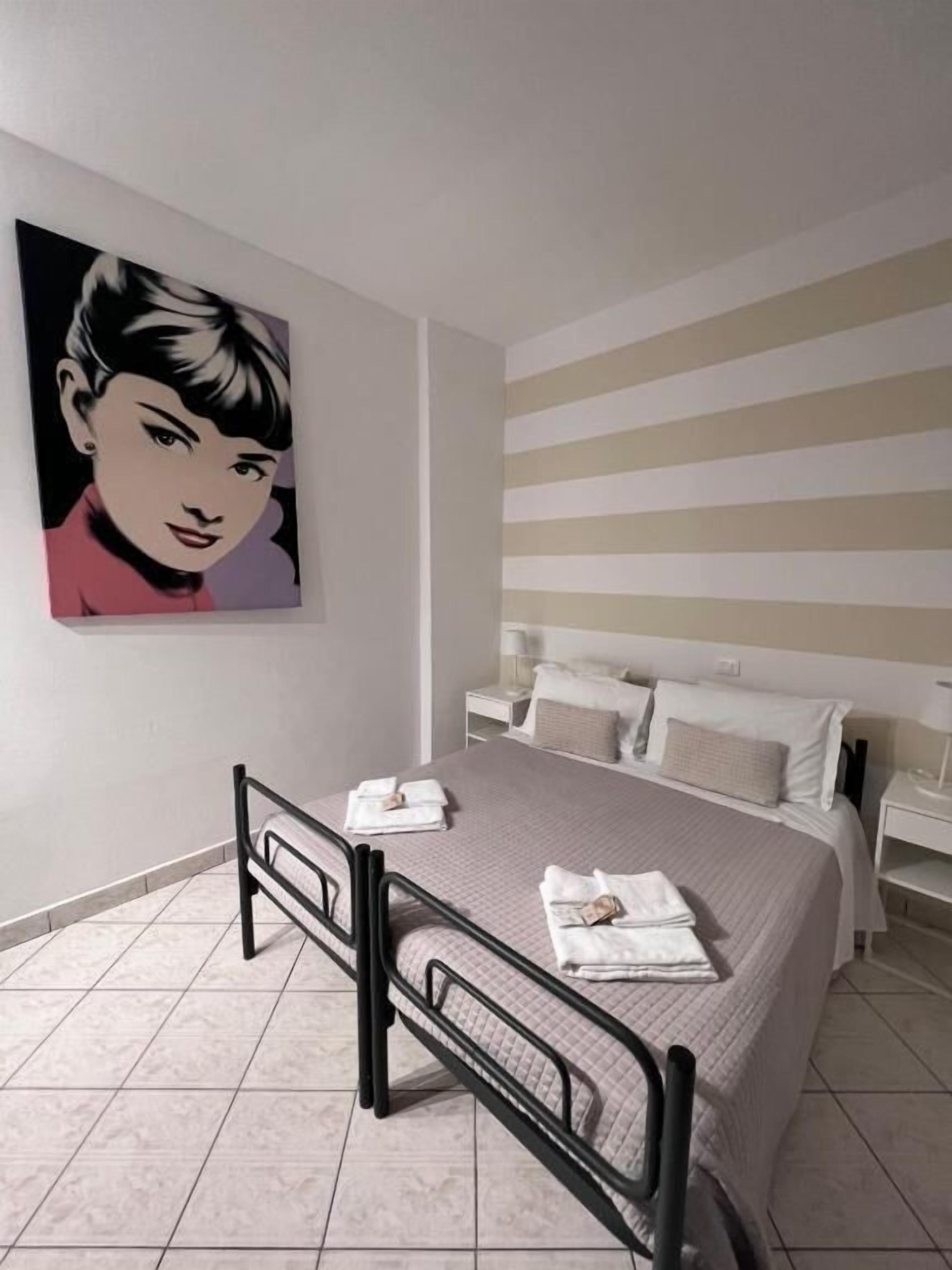 Un dormitorio con cama, mesita de noche, cuadro y ventana.