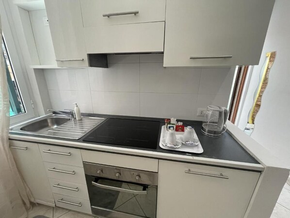 A compact kitchen with white cabinets, a stainless steel sink, a black countertop, and a small oven. - La Casetta (La Spezia)