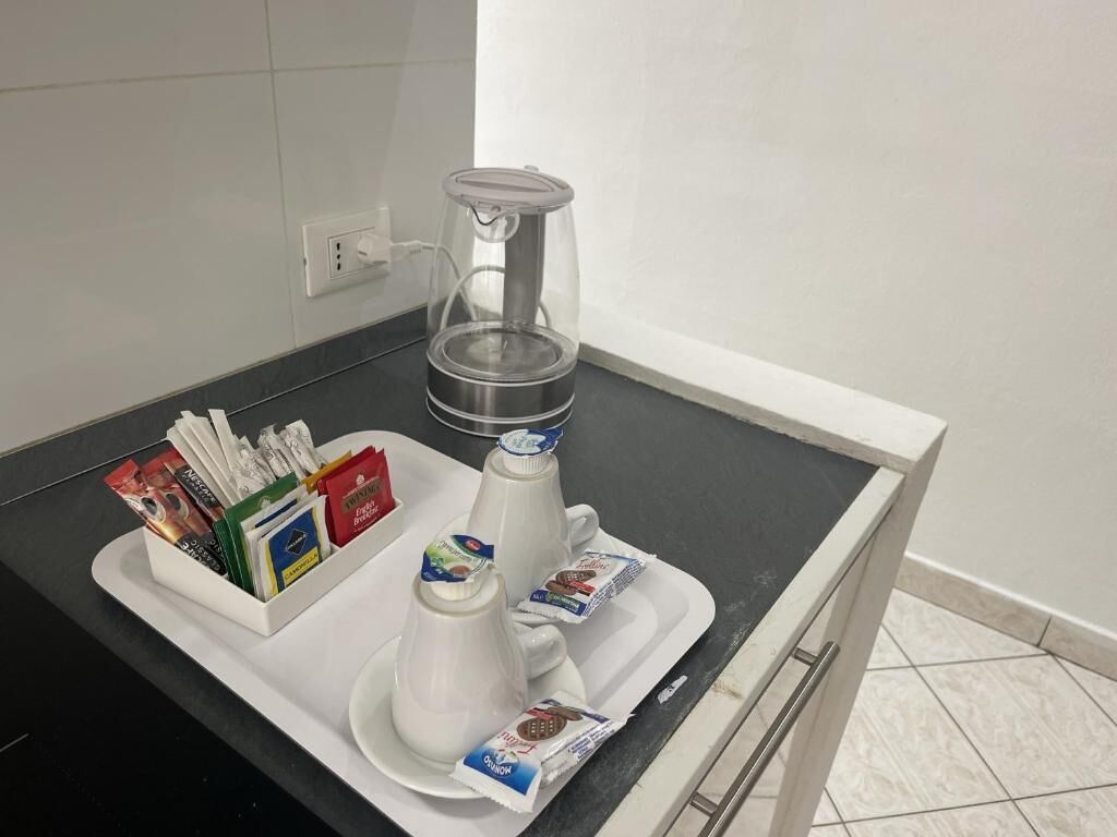 Una encimera de cocina con una cafetera, una bandeja con cápsulas de café y un recipiente con sobrecitos de azúcar.