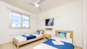 Una camera d'albergo con due letti singoli, una ventola a soffitto, una grande finestra e un'opera d'arte appesa al muro.
