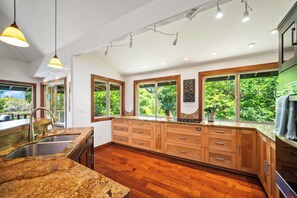 Eine moderne Küche mit Granit-Arbeitsplatten, Holzschränken und großen Fenstern mit Blick ins Grüne.