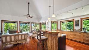 A modern kitchen with a bar area, large windows, and a ceiling fan. - Ohana Kai, Luxe Princeville home w/ AC (Princeville)