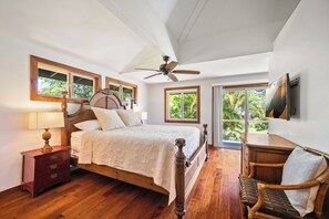 Ein Schlafzimmer mit einem Holzbett, einem Nachttisch, einem Stuhl, einem Deckenventilator und einem großen Fenster mit Blick auf Grünflächen.