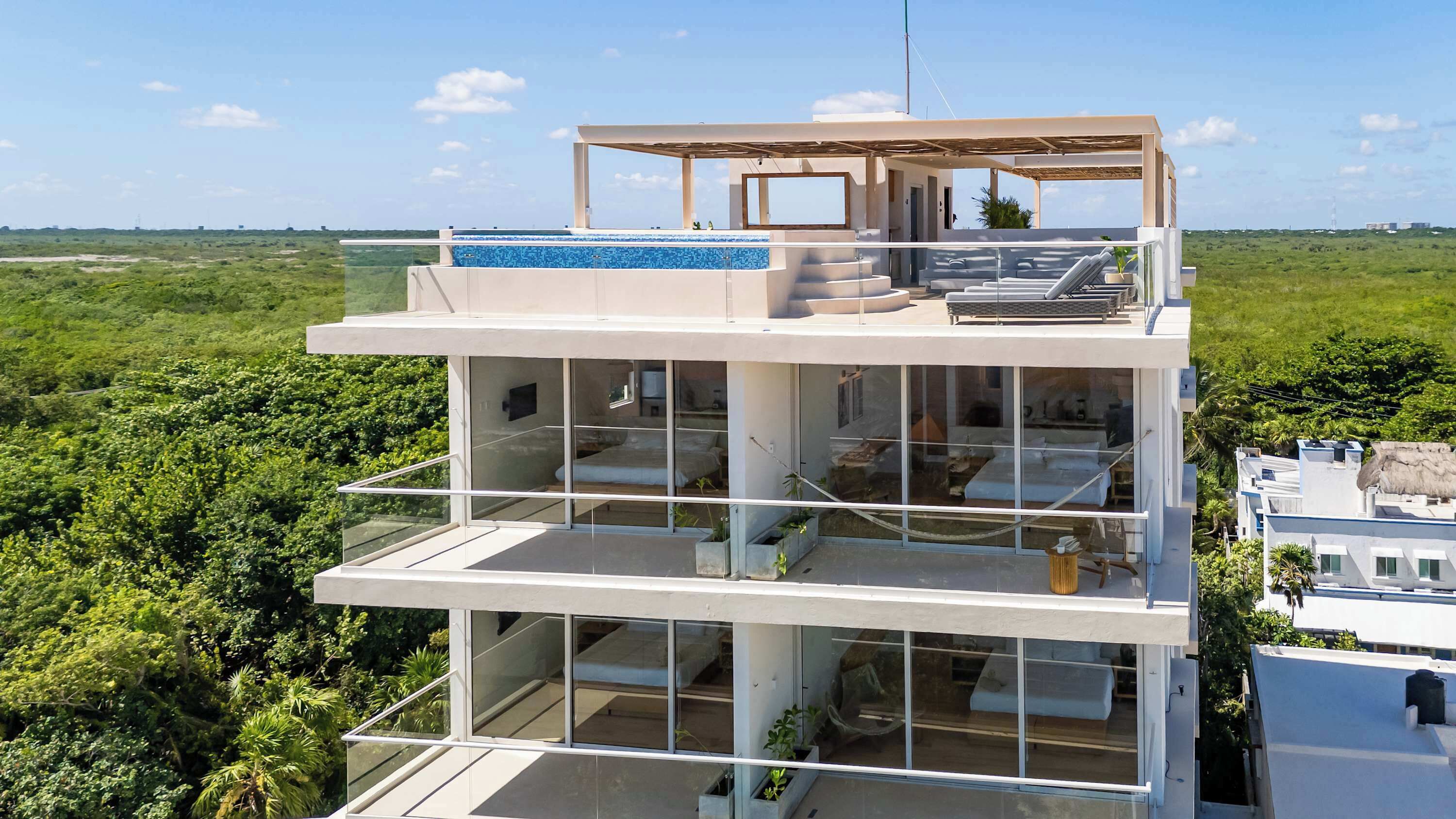 A modern multi-story building with a rooftop pool, large glass windows, and a balcony with outdoor seating.