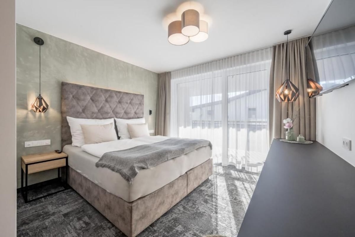 Ein modernes Schlafzimmer mit einem großen Bett, Nachttischen, einem Schreibtisch und Blick ins Freie.