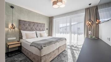 A modern bedroom with a large bed, bedside tables, a desk, and a view of the outdoors.