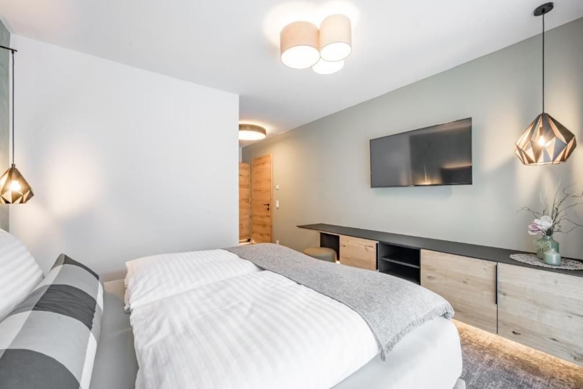 Ein modernes Schlafzimmer mit einem Bett, Nachttischen, einem Fernseher und einem Holzkasten.