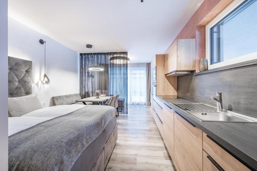 A modern hotel room with a bed, a dining area, and a kitchenette.