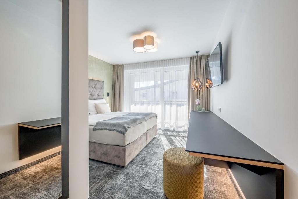 Une chambre d’hôtel moderne équipée d’un lit, d’un téléviseur à écran plat fixé au mur, d’une table de chevet et d’une grande fenêtre avec des rideaux.
