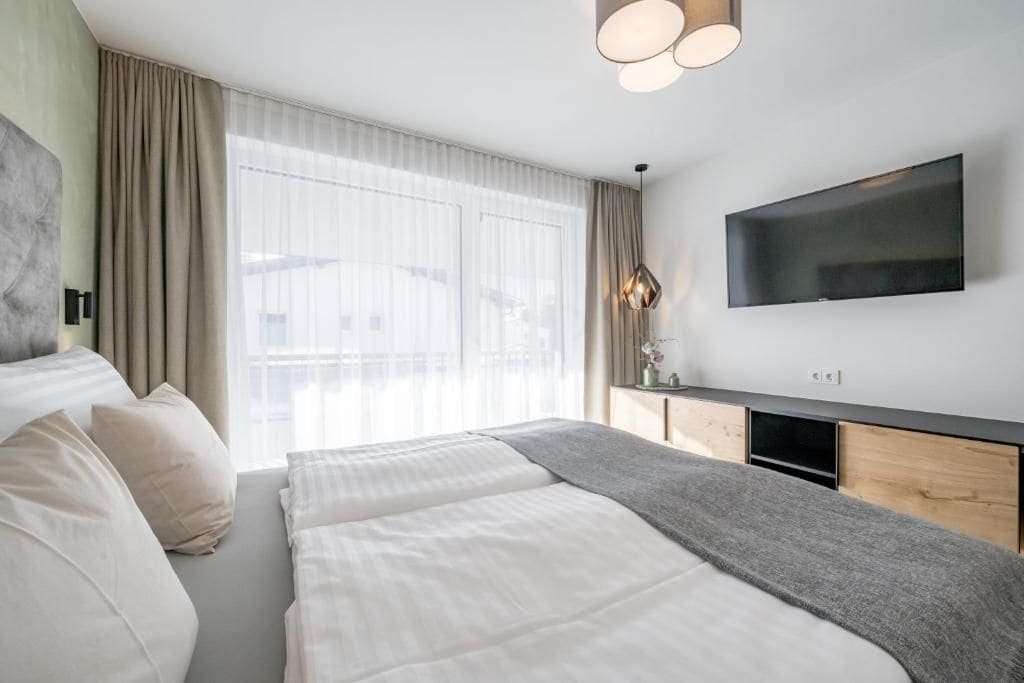 Une chambre d’hôtel moderne dotée d’un grand lit, d’un téléviseur à écran plat fixé au mur et d’une grande fenêtre avec des rideaux.