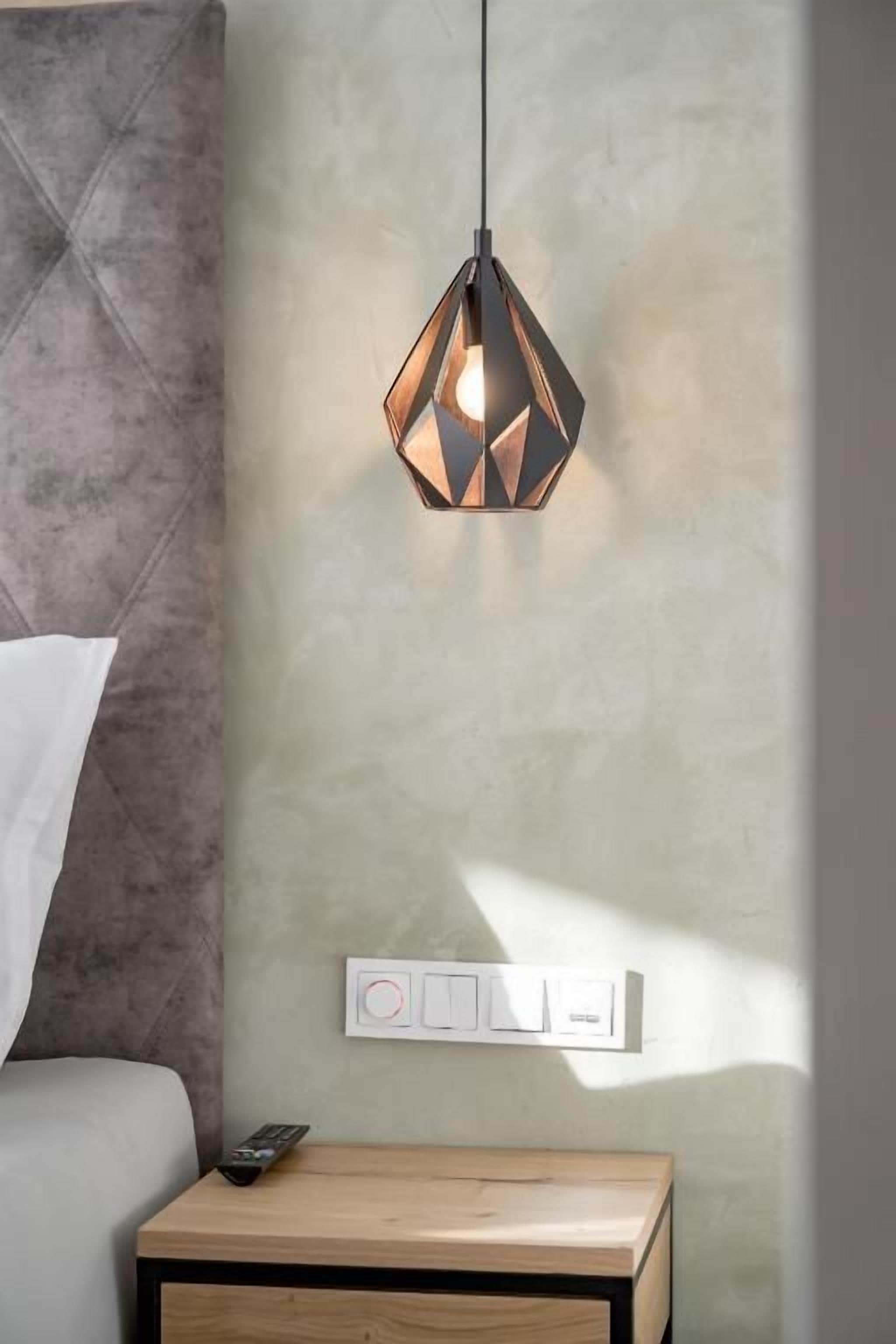 A modern bedroom with a geometric pendant light, a bedside table with a remote control, and a wall-mounted light switch.