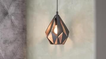 A modern bedroom with a geometric pendant light, a bedside table with a remote control, and a wall-mounted light switch.