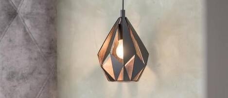 A modern bedroom with a geometric pendant light, a bedside table with a remote control, and a wall-mounted light switch.