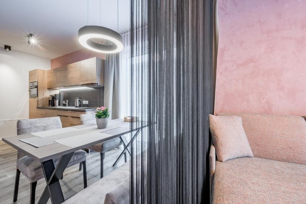 Ein moderner Wohnraum mit Essbereich, Küche und einem großen Fenster mit Vorhängen.