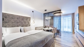 A modern hotel room with a large bed, a small dining table, and a view of the city through the window. - MYALPS Jordans Lodge (Oberried)