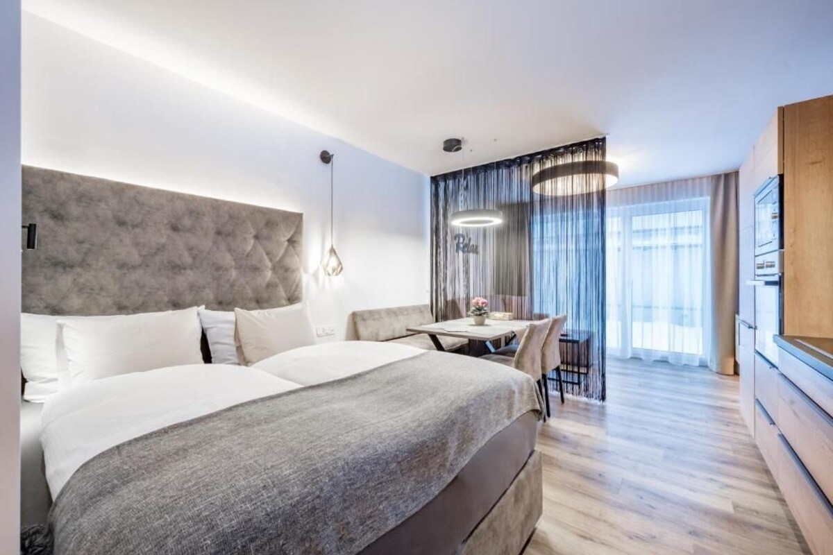 Ein modernes Hotelzimmer mit einem großen Bett, einem kleinen Esstisch und Blick auf die Stadt durch das Fenster.