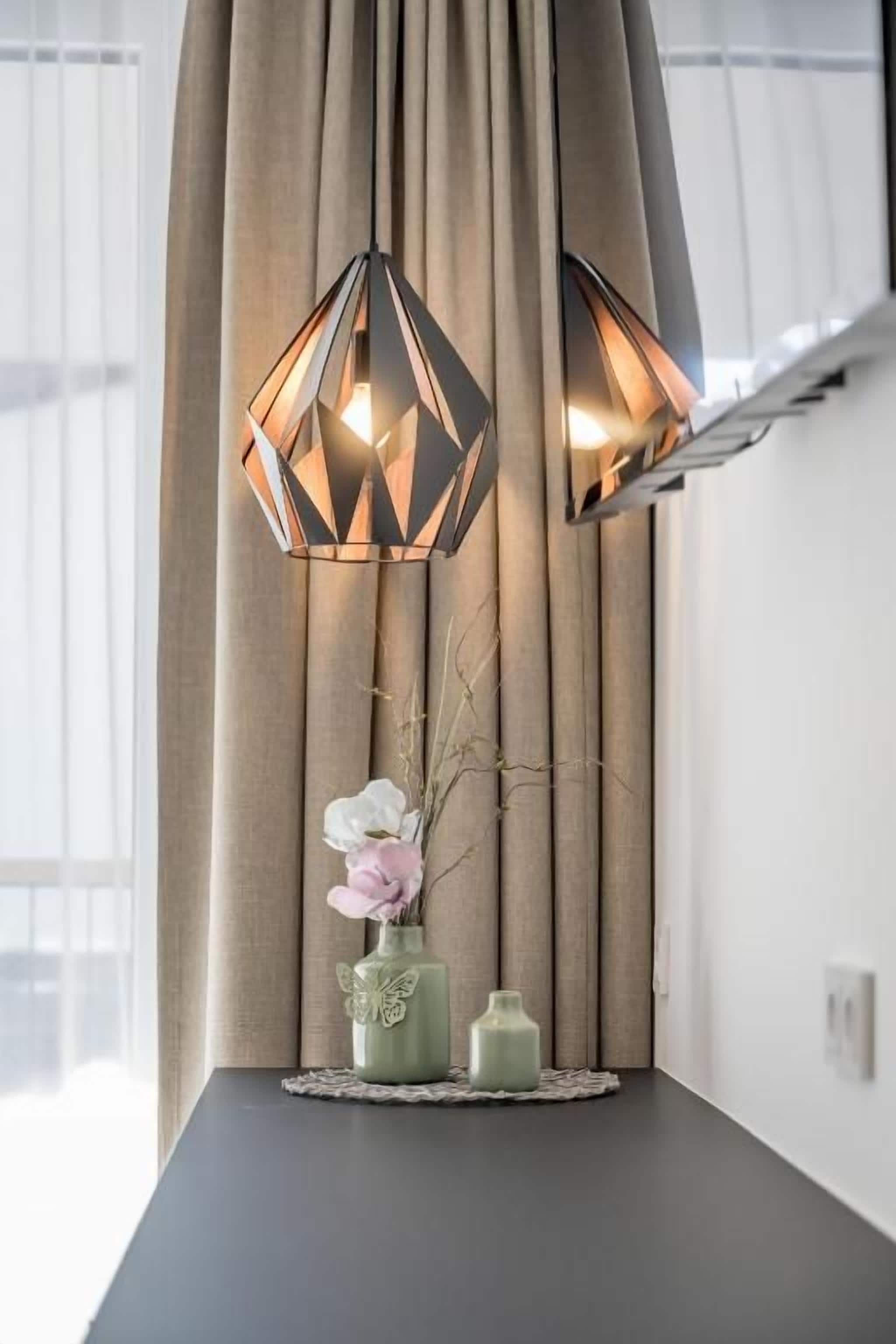 Una habitación con una mesa de color oscuro, un florero con flores y dos lámparas colgantes de diseño geométrico.
