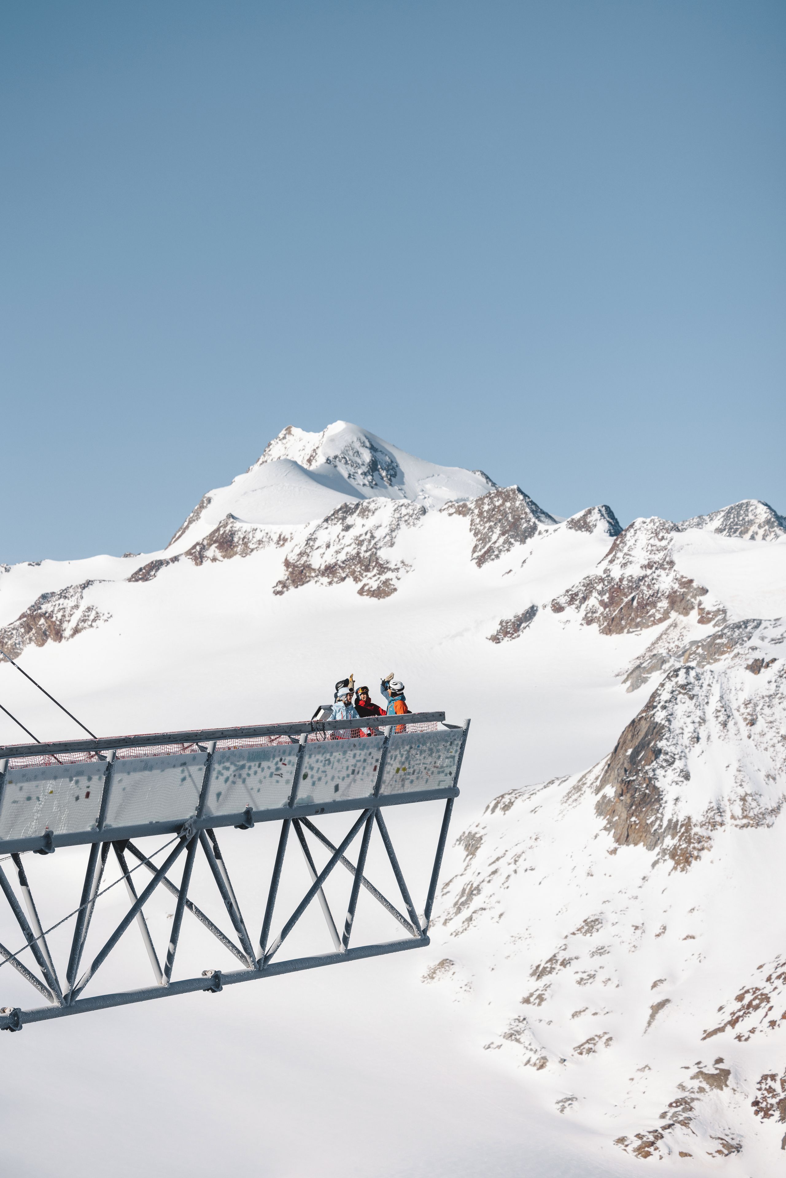 A metal structure with a metal railing, snow-covered mountains in the background, and a clear sky.