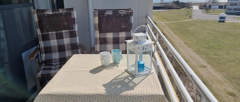 A balcony with a table, two chairs, a white lantern, and a view of the sea and buildings.