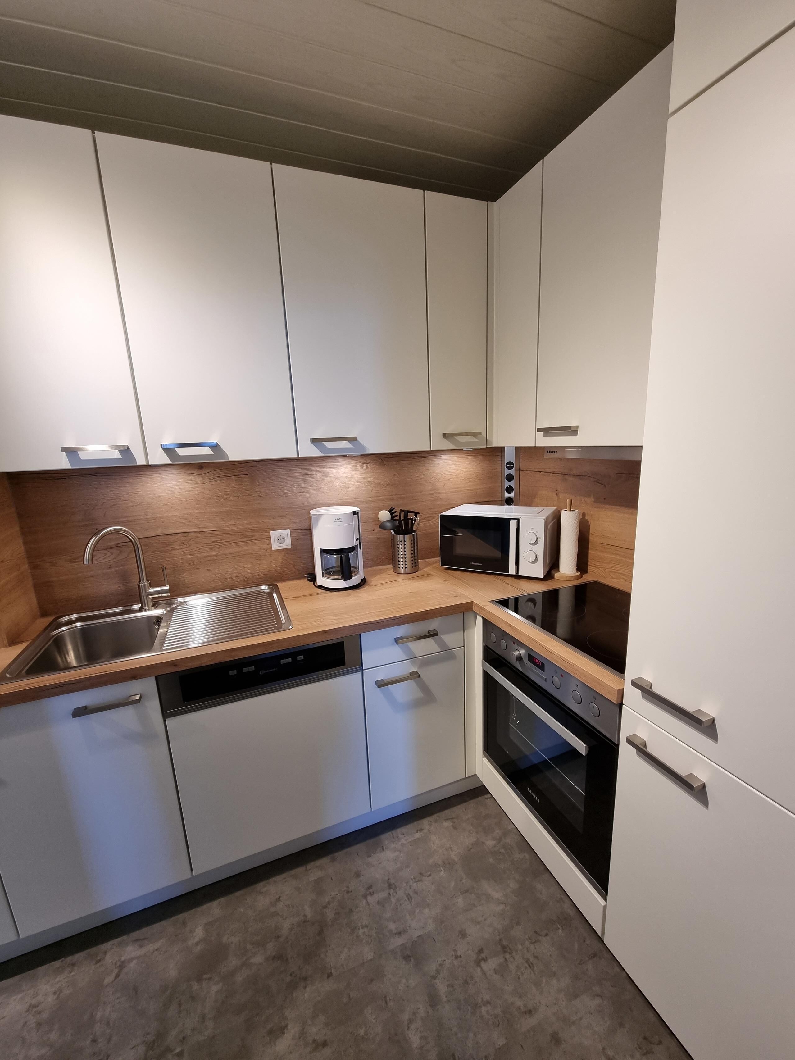 A modern kitchen with white cabinets, a wooden countertop, stainless steel appliances, and a dishwasher.