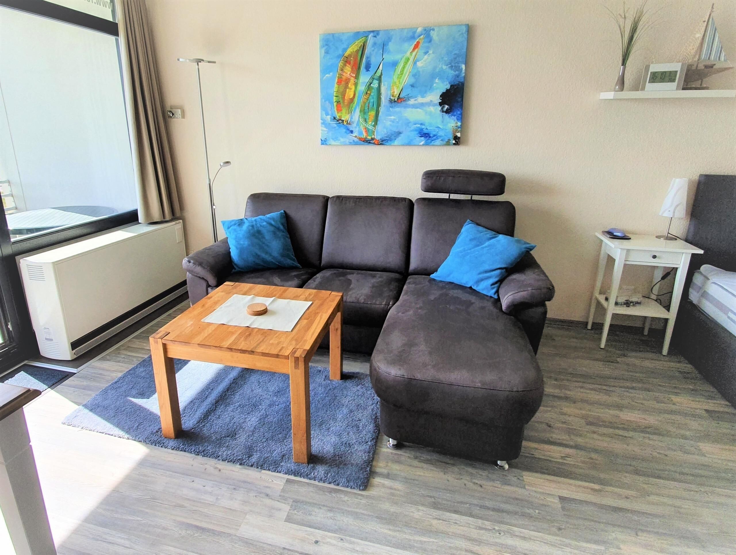Een woonkamer met een hoekbank, een houten salontafel, een schilderij aan de muur, en een bijzettafeltje met een lamp.
