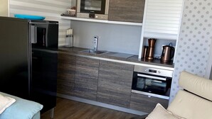 A compact living space with a kitchenette, a dining area with a table and chairs, and a sofa. - Vacation apartment Fehmarn sea view - terrace & beach near Fehmarnsund (Fehmarn)