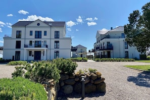 A multi-story residential building with a symmetrical facade, a central entrance, and a gravel driveway. - Vacation apartment Fehmarn sea view - terrace & beach near Fehmarnsund (Fehmarn)