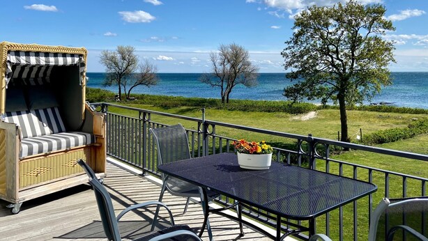 A deck with a wicker sofa, metal chairs, and a table with a flower pot. - Vacation apartment Fehmarn sea view - terrace & beach near Fehmarnsund (Fehmarn)