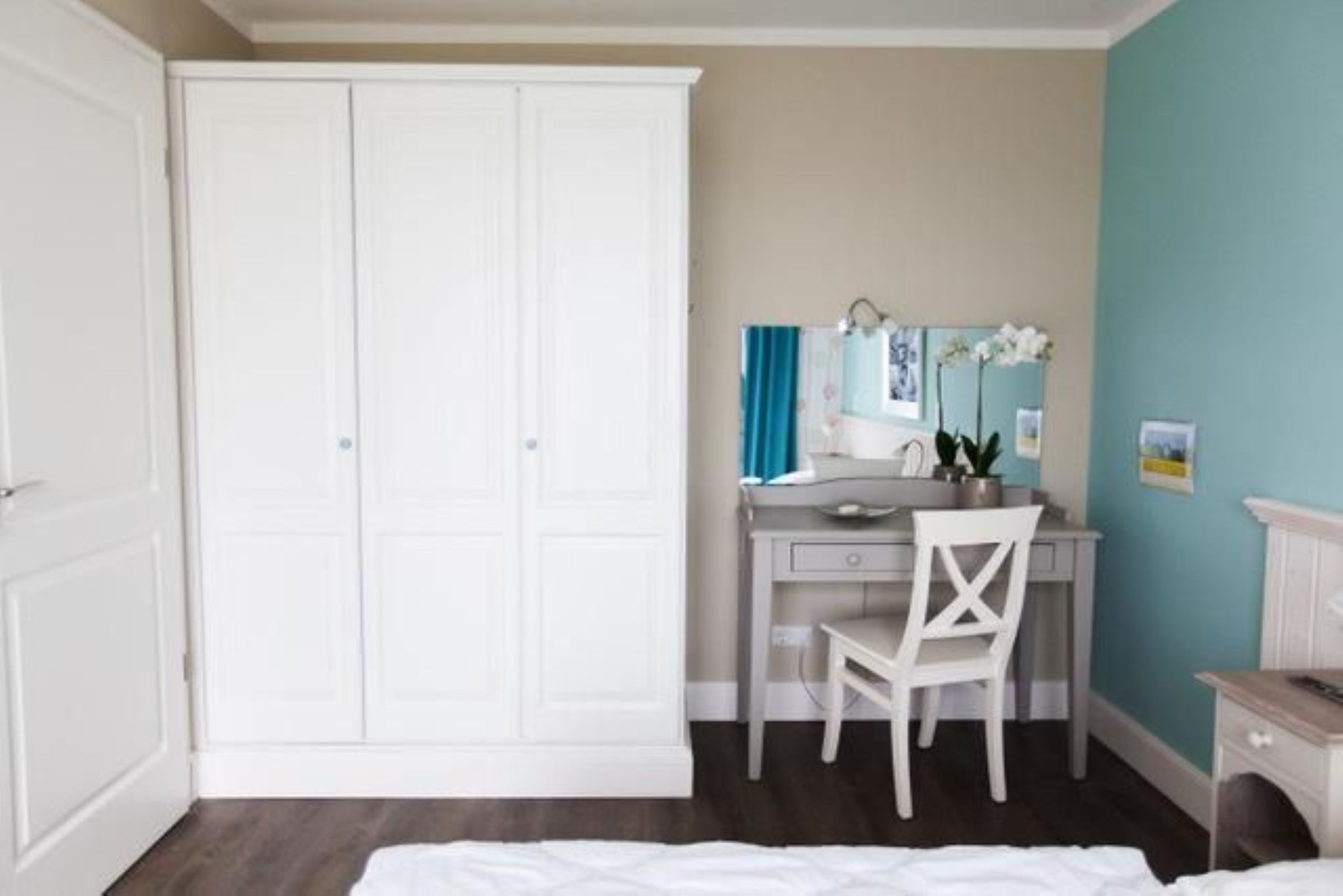 A bedroom with a bed, a desk with a chair, a wardrobe, and a mirror.