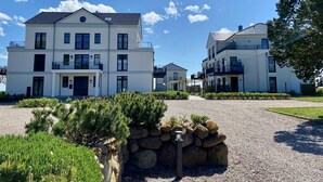 A modern multi-story residential building with a symmetrical facade, multiple balconies, and a gravel driveway. - Vacation apartment Fehmarn sea view - terrace & beach near Fehmarnsund (Fehmarn)