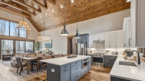 Une cuisine spacieuse dotée d’un grand îlot central, d’appareils électroménagers modernes et d’un plafond en bois rustique.