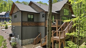 Une cabane avec des fondations en pierre, une terrasse en bois et un escalier menant à un balcon.