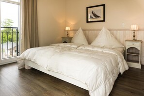 A bedroom with a large bed, two bedside tables with lamps, a window with curtains, and a framed picture on the wall. - An unforgettable vacation on the Baltic Sea: ocean views and pure comfort!   (Fehmarn OT Fehmarnsund)